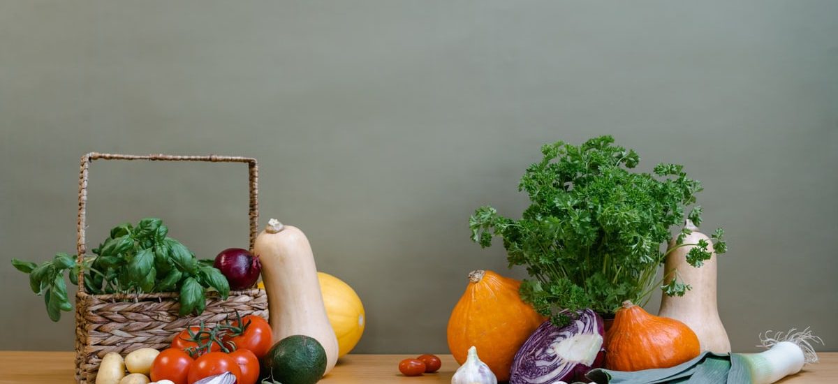 A variety of fresh vegetables including squash, tomatoes, and greens arranged on a wooden table.