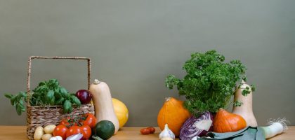 A variety of fresh vegetables including squash, tomatoes, and greens arranged on a wooden table.