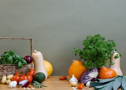 A variety of fresh vegetables including squash, tomatoes, and greens arranged on a wooden table.